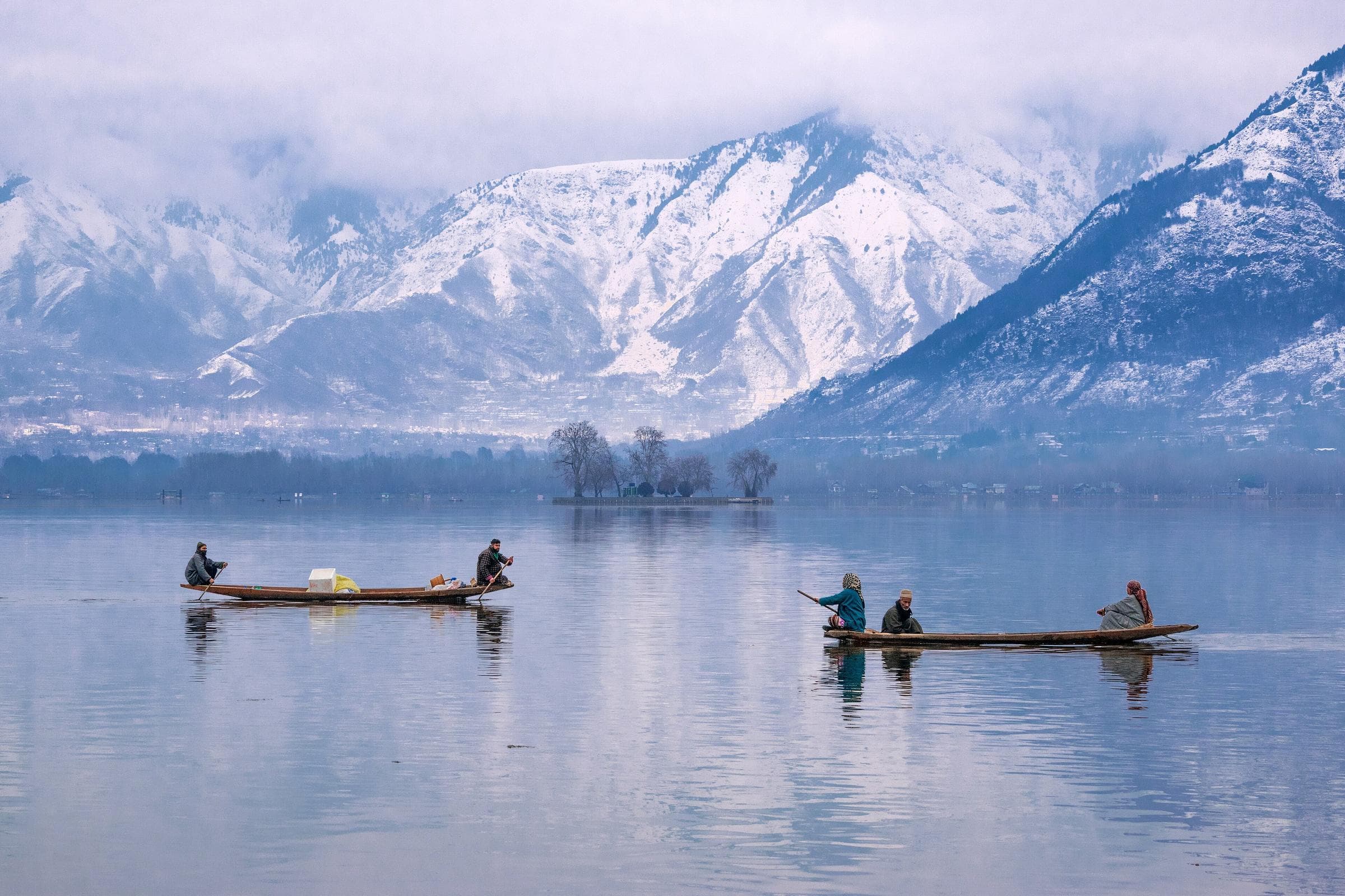 Two shikaras crossing a still Dal Lake, with snow-covered mountains behind.