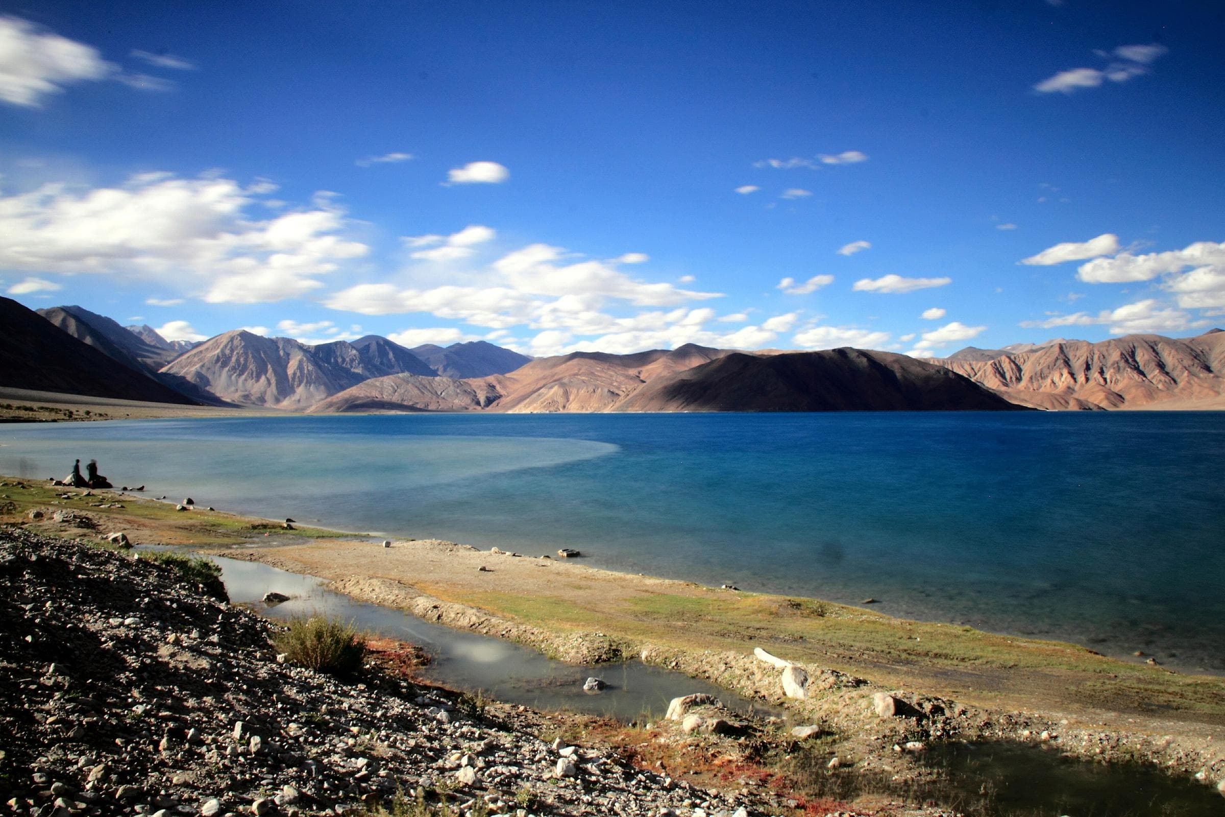 The blue water of Pangong Tso under white clouds, with bare brown mountains on the far shore.